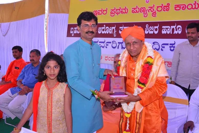 A memento being offered to a garlanded Swamiji at the punyasmarane observance and health camp